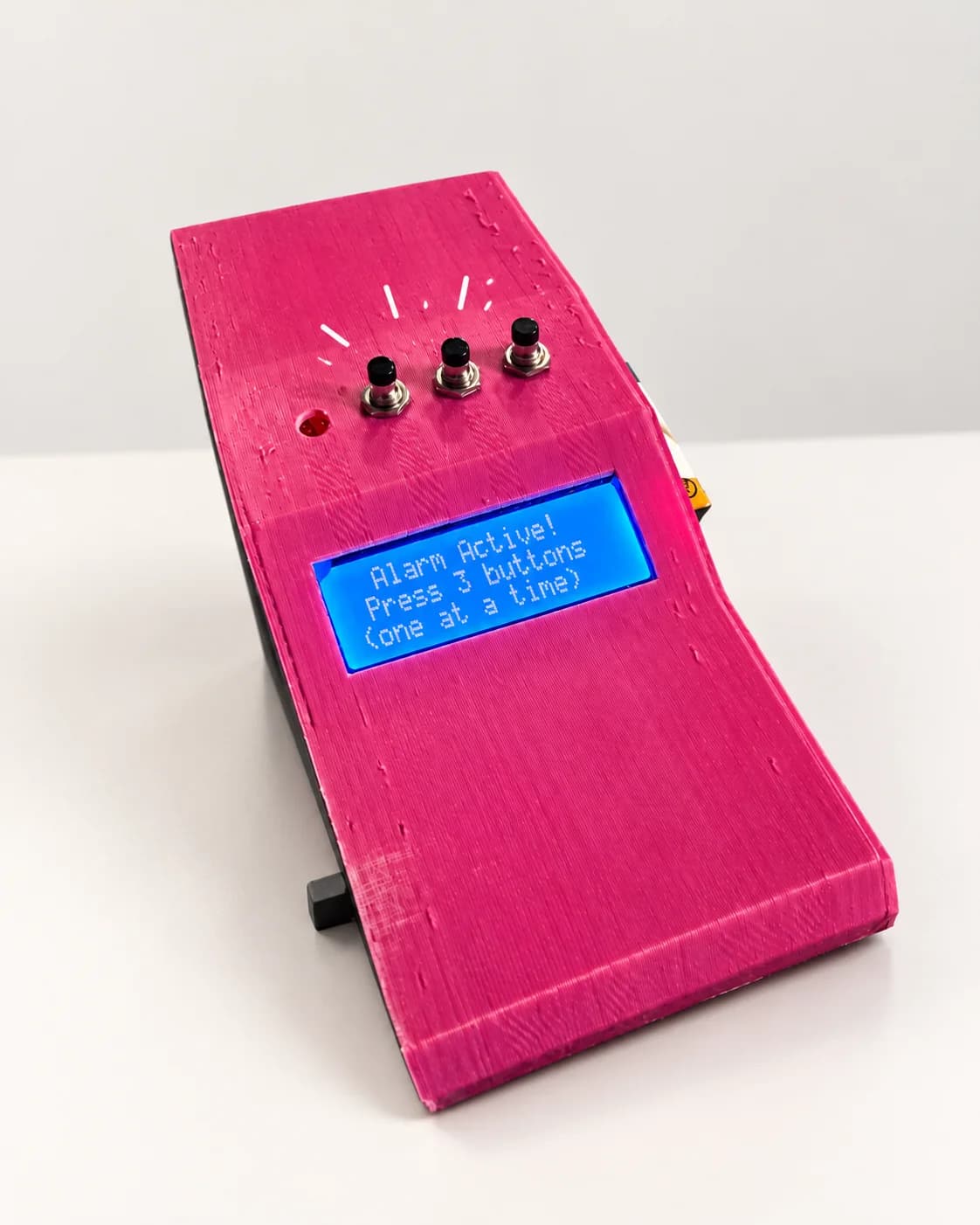 A pink alarm clock whose screen reads: Alarm active! Press 3 buttons, one at a time